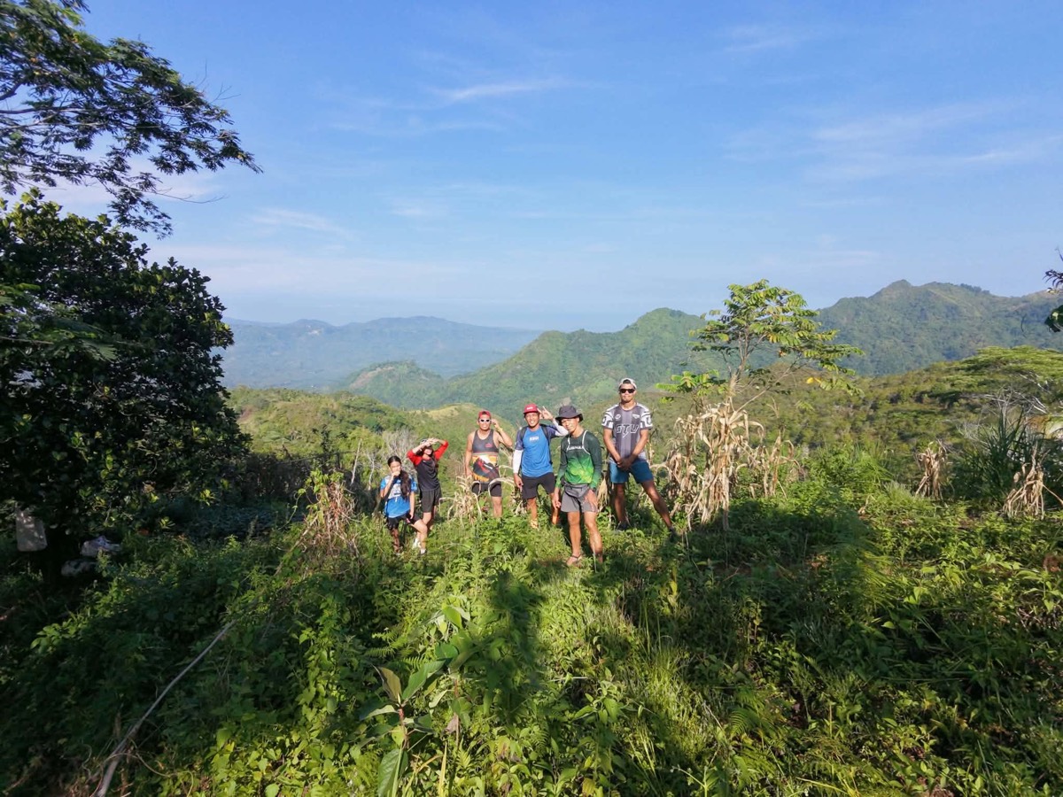 Hikers standing on a green ridge with mountains and the sea behind